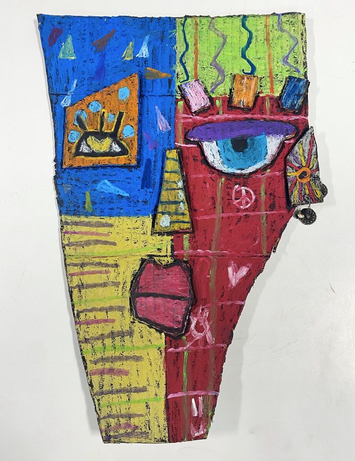 A young artist's mask inspired by Kimmy Cantrell. The mask is a face in the shape of Vermont and has four main quadrants of color, from top left – blue with an orange eye, green with swirls of color, red with a white and purple eye, yellow with multi-colored lines.
