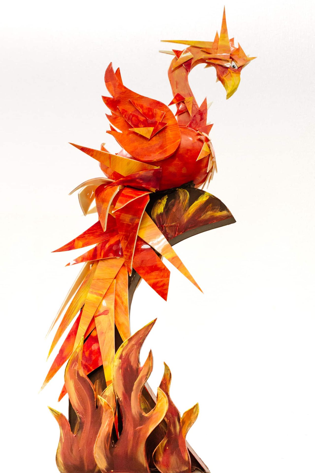 A large chocolate sculpture featuring a Phoenix sitting on top of abrtract red shared that look like flames. The feathers of the Phoenix mimick the same shape and colors of the flames.