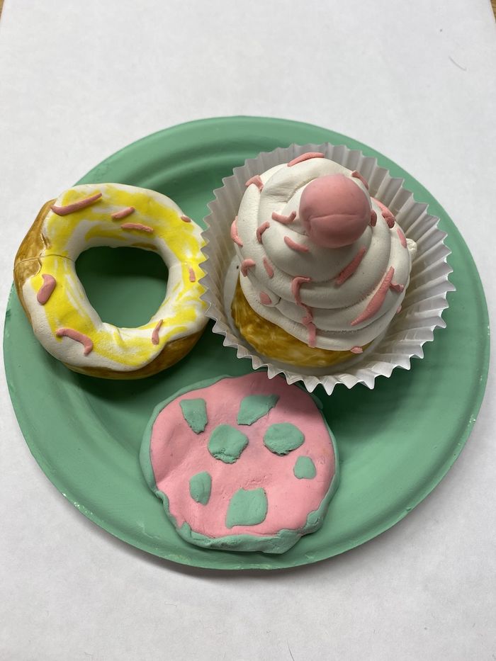 A top down view of a sculpted food out of air dry clay including a pizza, a bagel, and a cupcake.