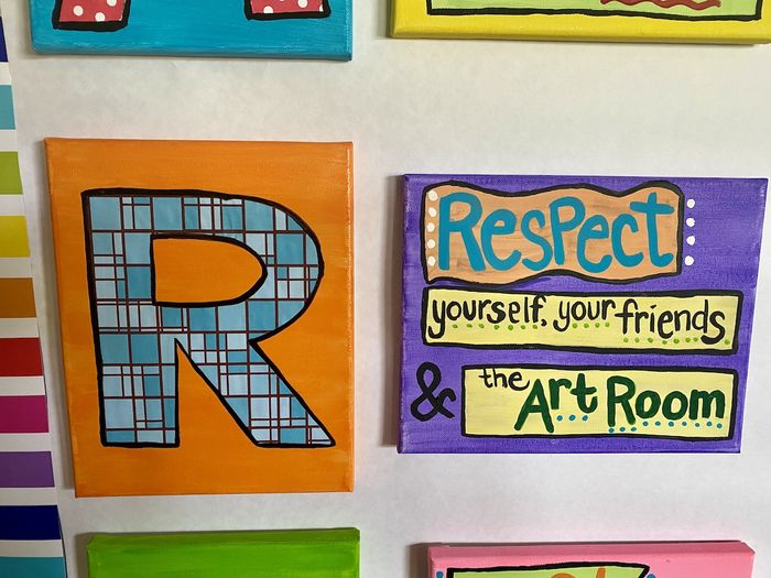 Two painted canvases, on the left a large letter R on an orange background. On the right the phrase 'Respect yourself, your friends, and the art room.'